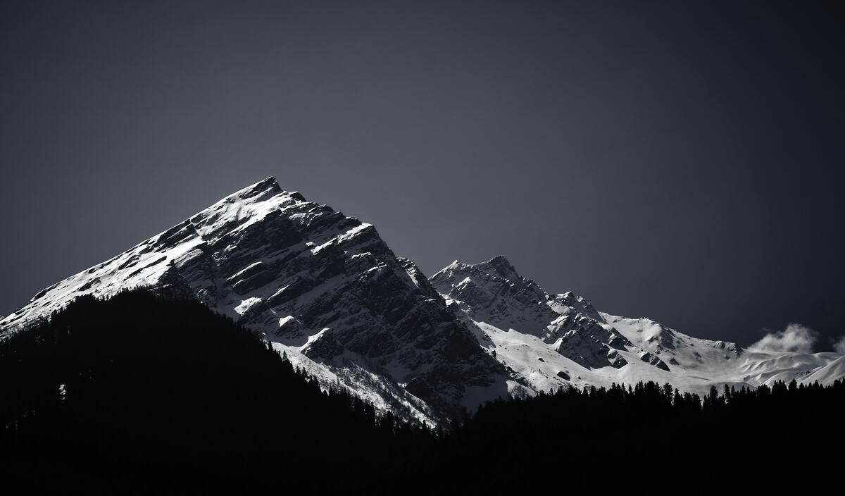 A snow-lit ridge above a black forest, under a graphite sky